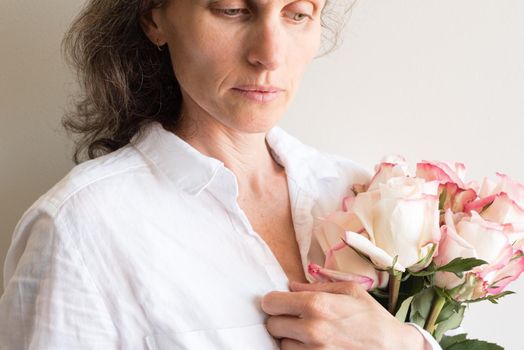Middle aged woman holding roses and looking pensive (cropped)