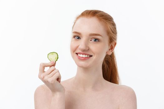 Close up beauty portrait of a smiling beautiful half naked woman holding cucumber slices at her face isolated over white background.