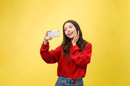 Smiling young girl making selfie photo on smartphone over yellow background.