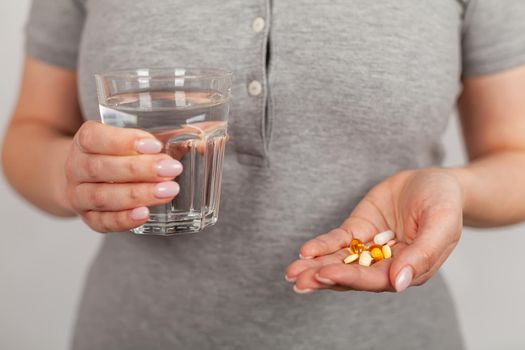 Female hands hold pills and a stock of water. Health care, medical supplement concept. Sick girl holding medicine to recover her headache. Woman holds a glass of water. Healthcare concepts.