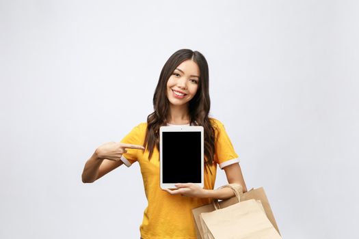 Portrait of woman in summer dress holding packages bags with purchases after online shopping, using tablet pc pad computer isolated on white background. Copy space for advertisement.