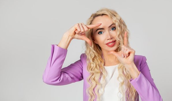 Creative, pretty blonde curly woman, photographer or designer looking for the perfect angle of view from the point of view, making hands framed and smiling