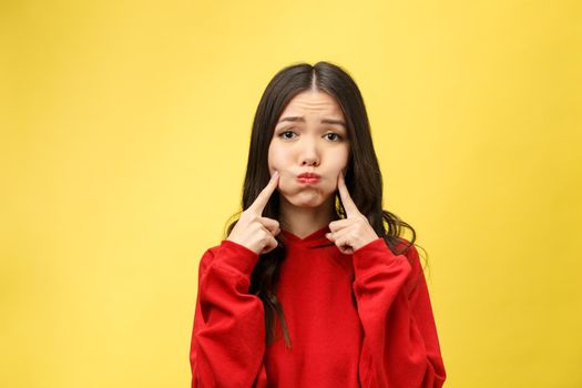 Portrait of good looking young attractive woman has curious gaze at camera, keeps finger on chin, listens attentively interlocutor, poses against yellow background. People and happiness concept