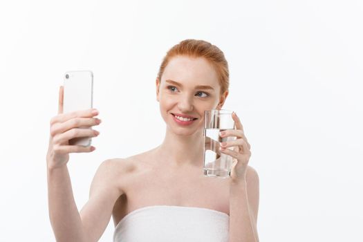 Happy smiling young woman with healthy skin reading and writing in mobile phone sms and drinking clean water. Consulting the diet. Closeup portrait.