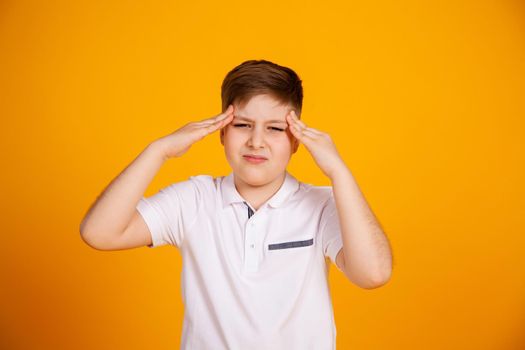 A boy with a headache. Caucasian child on a yellow background suffering from headache and migraine. Hands on the head.