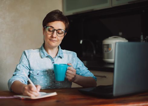 Working at home. Female entrepreneur working from home writing to-do list with laptop and coffee in the morning in the kitchen. Work from home.