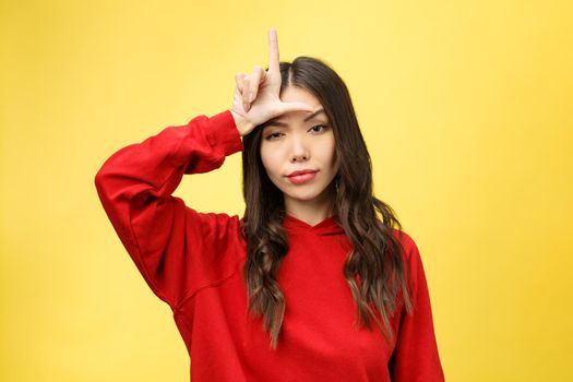 Pretty young woman showing phone sign with her fingers. Colorful studio portrait with yellow background