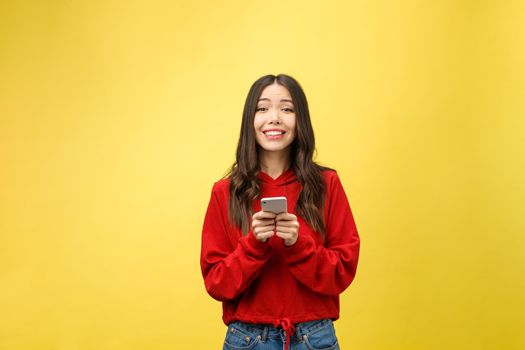 Young beautiful happy woman using smart phone. Isolated on yellow background.