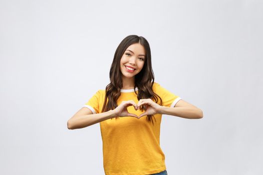 Portrait of a smiling young asian woman showing heart gesture with two hands and looking at camera isolated over white background