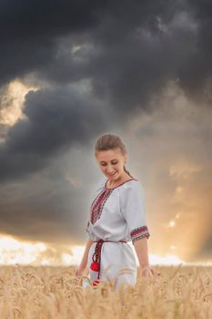 girl in an embroidered shirt on a wheat field and a sunset sky