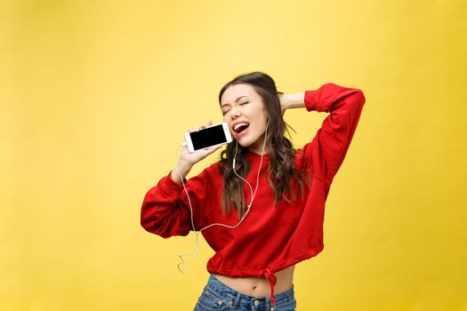 Portrait of a happy woman listening music in earphones and dancing isolated on a yellow background.