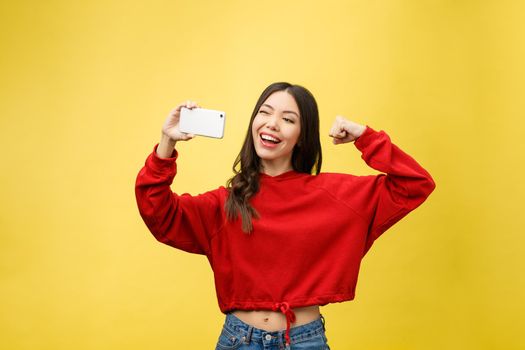 Smiling young girl making selfie photo on smartphone over yellow background.