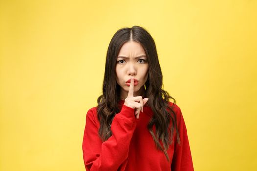 Young woman over yellow wall showing a sign of silence gesture putting finger in mouth.