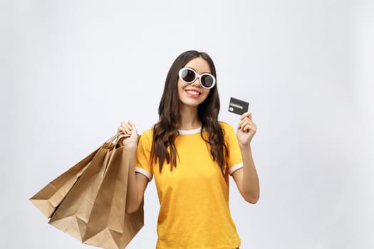 Close-up portrait of happy young brunette woman in sunglasses holding credit card and colorful shopping bags, looking at camera, isolated on white background.