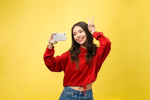 Smiling young girl making selfie photo on smartphone over yellow background.