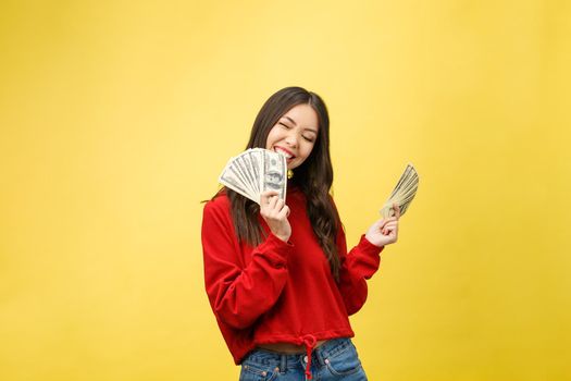 Closeup of young beautiful woman with us dollar money in hand over yellow background, with copy space.