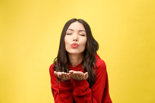 Beautiful young Asian woman blow a kiss on yellow background