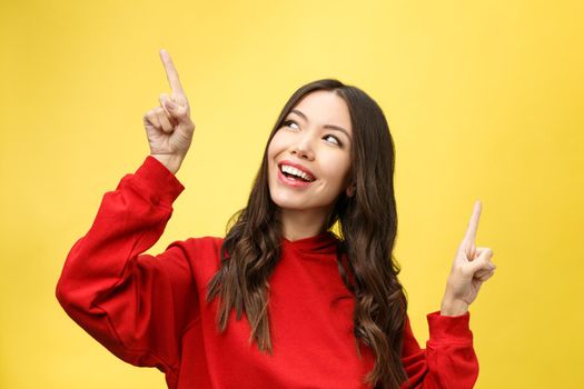 Young beautiful asian woman pointing to copyspace, isolated on yellow background.