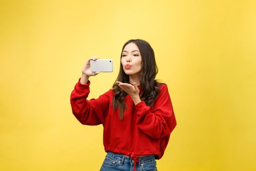 Smiling young girl making selfie photo on smartphone over yellow background.