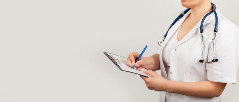 Female doctor writes with a pen a document on a tablet, writes a medical history. The concept of healthcare, medicine and pharmacy.