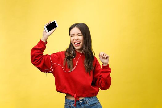 Portrait of a happy woman listening music in earphones and dancing isolated on a yellow background.
