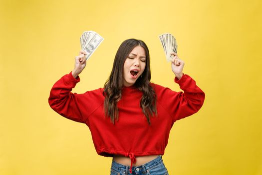 Closeup of young beautiful woman with us dollar money in hand over yellow background, with copy space.