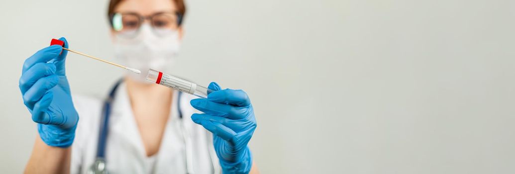Test for coronavirus Covid-19. Female doctor or nurse doing lab analysis of a nasal swab in a hospital laboratory. Medical technologist holding a COVID-19 smear kit, wearing protective gloves from