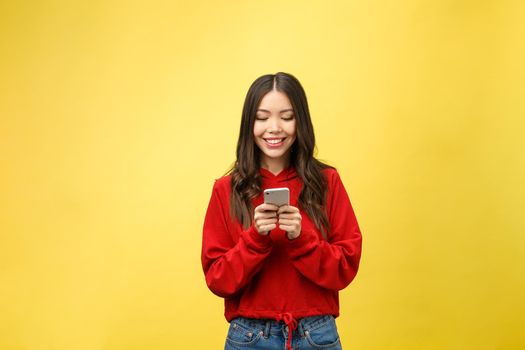 Young beautiful happy woman using smart phone. Isolated on yellow background.