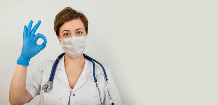 Medical worker wearing a protective mask and showing ok sign. Woman wears a surgical mask from the crown virus, studio portrait