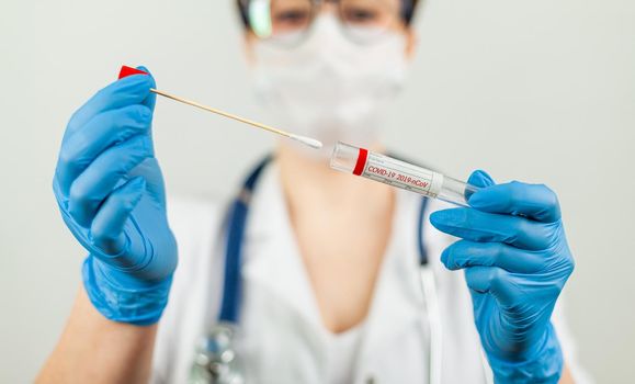 Test for coronavirus Covid-19. Female doctor or nurse doing lab analysis of a nasal swab in a hospital laboratory. Medical technologist holding a COVID-19 smear kit, wearing protective gloves from