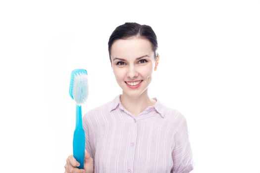 joyful woman in a purple shirt holding a huge blue toothbrush in her hands, white background. High quality photo