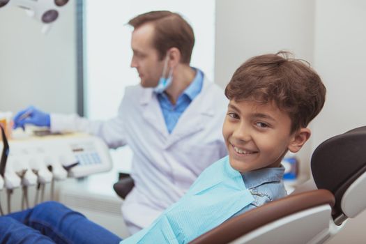 Childrens dentistry. Lovely cheerful boy smiling to the camera, waiting for dental checkup by his orthodontist, copy space