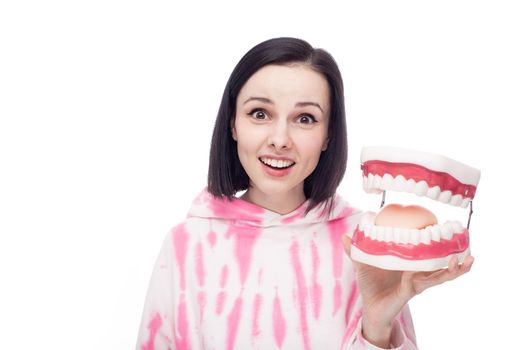 smiling woman in a pink hoodie holds a dental jaw in her hand, white background. High quality photo