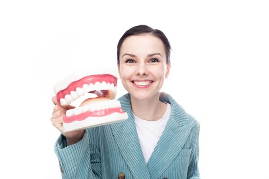 joyful woman in blue velvet jacket holds a huge jaw with teeth in her hand, white background. High quality photo