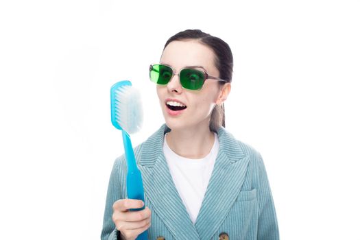 funny woman in green glasses holds a big toothbrush in her hand, white background. High quality photo