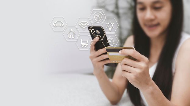 Asian woman holding mobilephone and credit card with various icon concept payment pay for food house, car, water, electricity, telephone bills, online shopping concept. With copy space