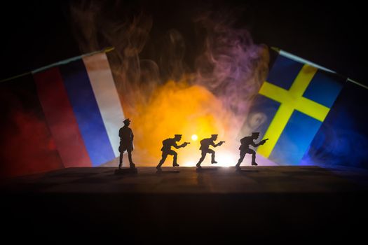 Flags of Sweden and Russia on dark background. Conceptual image of war between Russia and Sweden using toy soldiers and national flags . Selective focus