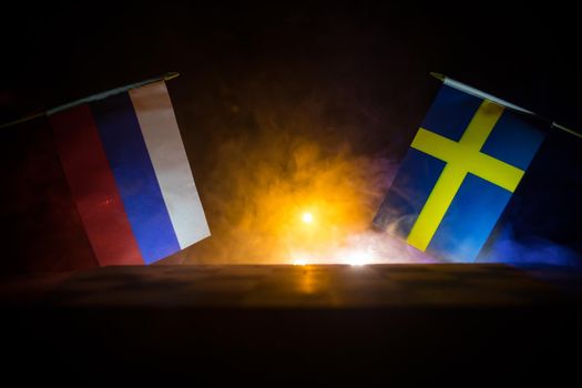 Flags of Sweden and Russia on dark background. Conceptual image of war between Russia and Sweden using national flags . Selective focus