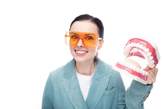 joyful woman in orange glasses, velvet jacket holds a huge jaw with teeth in her hand, white background. High quality photo