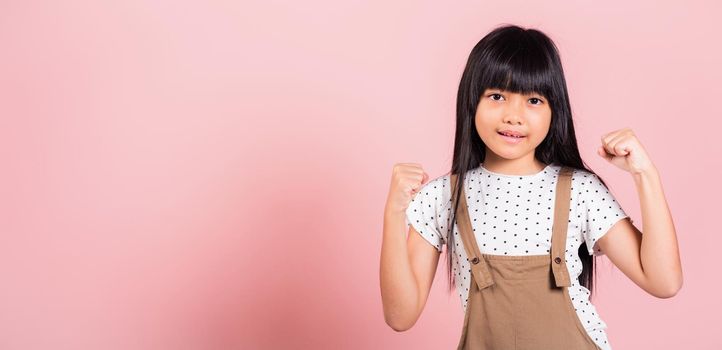 Yes ! Asian little kid 10 years old celebrating great success with arms raised at studio shot isolated on pink background, Happy and excited child girl positive smiling cheerful