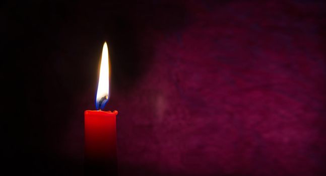 Single red candle burning alone in the dark red background. Conceptual image of peace, love, hope or patience in a panorama banner with free copy space