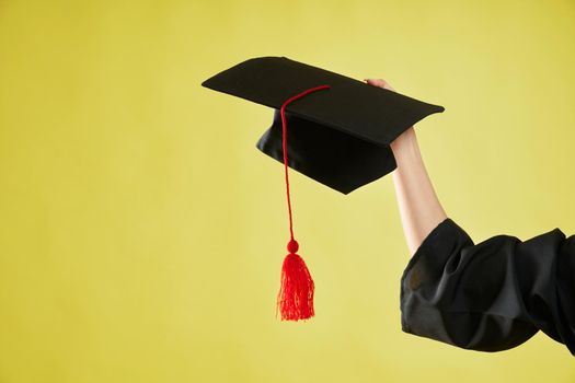 Close up of hand holding, showing mortarboard. Female student with bachelor, master degree graduating from college, university, high school. Isolated on green studio background,