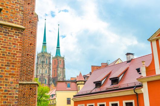 View of two towers with spires of Cathedral of St. John the Baptist catholic church and tiled roofs of buildings with blue cloudy sky in old historical city centre, Ostrow Tumski, Wroclaw, Poland