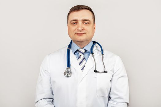 Portrait of smiling young male doctor with a stethoscope around neck standing within a white coat, isolated on gray background