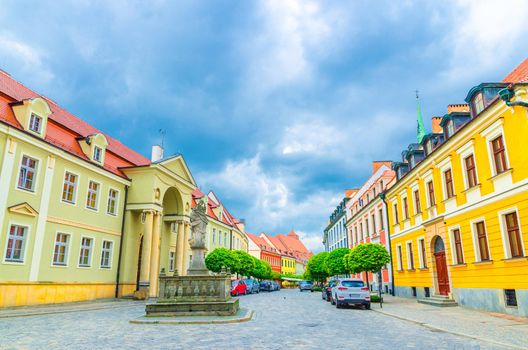 Cobblestone street with colorful buildings and Statue of Madonna and Child monument with blue cloudy sky background in old historical city centre, Ostrow Tumski, Wroclaw, Poland