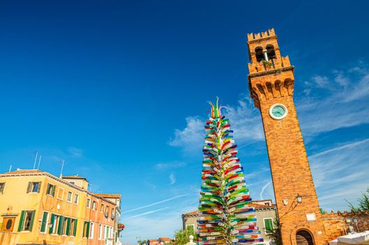 Murano clock tower Torre dell'Orologio of San Stefano church and Colorful christmas tree made of Murano Glass on Campo Santo Stefano square in Murano islands, Veneto Region, Northern Italy