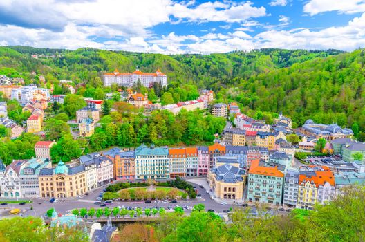 Karlovy Vary Carlsbad historical city centre top aerial view with colorful beautiful buildings, Slavkov Forest hills with green trees, blue sky white clouds background, West Bohemia, Czech Republic