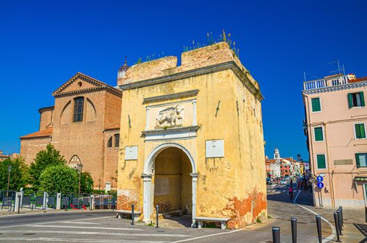 Porta Santa Maria o Porta Garibaldi gate and Cathedral Santa Maria Assunta Duomo catholic church in Chioggia town historical centre, blue sky background in summer day, Veneto Region, Northern Italy