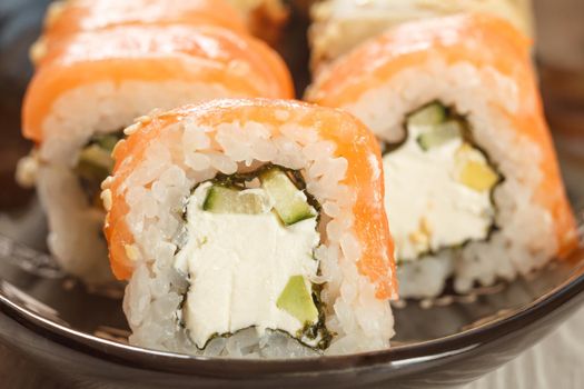 Close up Uramaki Philadelphia. Sushi rolls with salmon, nori, rice, Philadelphia cheese, pieces of avocado and cucumber on ceramic plate. Japanese cuisine. Shallow depth of field