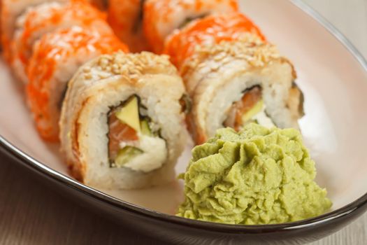 Close up wasabi and sushi rolls - Uramaki with Conger, Uramaki California on the background. Japanese cuisine. Shallow depth of field. Focus on wasabi